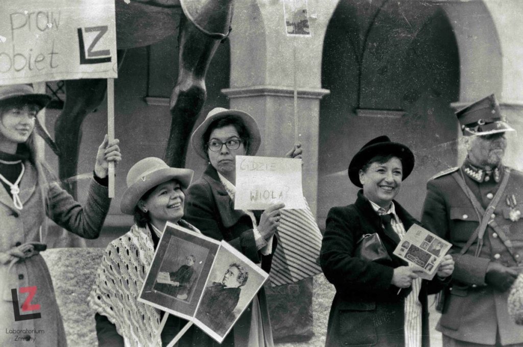 kobieta trzymająca w ręku dwa transparenty ze zdjęciami na kijach