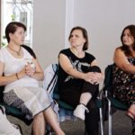 trzy kobiety prowadzą rozmowę siedząc na krzesłach